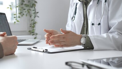 Doctor and patient are talking at office table during a consultation in a bright, modern clinic, close up of hands. Medicine and health care concept