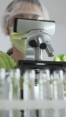 Close up of scientific precision involving green gloved hands adjusting microscope lens, blurred laboratory glassware highlighting medical investigation. Medicine, laboratory and science concept