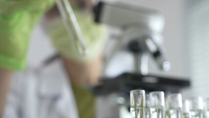 Close up of test tubes with a scientist analyzing plant samples in test tubes with a microscope in a laboratory at the background. Medicine, health care and science concept