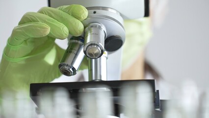 Close up of green gloved hands of a scientist adjusting a microscope in a laboratory, emphasizing the significance of scientific research and analysis. Medicine, healthcare and science concept