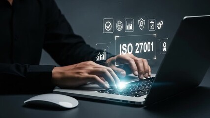 Person typing on laptop with iso 27001 graphic overlay and mouse on desk in dark studio setting - Powered by Adobe