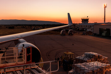 Sunset view of aircraft wing at airport with cargo and control tower visible in background