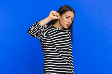 Fototapeta premium Knock-knock who is there. Confused Caucasian woman knocking door gesture asking who is at home feeling embarrassed, no idea being clueless and uncertain. Young adult girl isolated on blue background