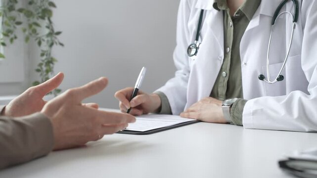 Doctor woman listening to male patient health concerns and writing a prescription during a consultation in a bright, modern clinic, close up. Medicine and health care concept