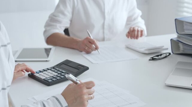 Two accountants collaborating in a well lit office, analyzing financial data and preparing reports with calculators and pens. Audit and taxes in business