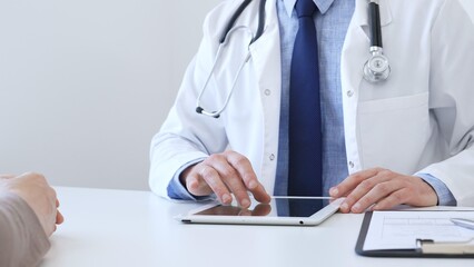 Close-up of doctor man showing information on tablet to patient woman during medical visit, explaining diagnosis and treatment options, providing medical consultation. Medicine concept