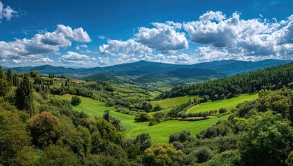 Naklejka premium Panoramic view of rolling green hills, lush forests, and a vibrant blue sky dotted with fluffy white clouds, showcasing a serene and picturesque landscape
