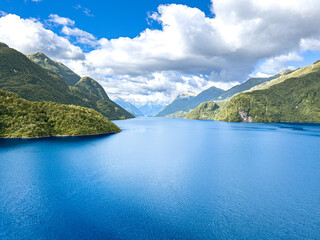 Stunning Milford Sound fjord with calm blue waters and lush green hills under a vast cloudy sky, New Zealand