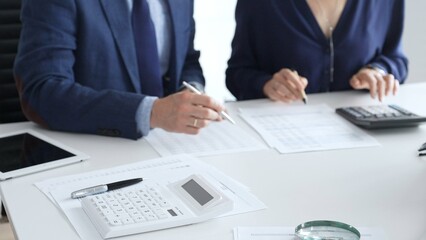 Calculator and magnifying glass over financial documents opposite financial team analyzing data, reviewing reports, collaborating at modern office workspace, close up view. Audit and taxes