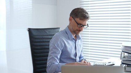 Male professional accountant calculating invoices and managing bills while reviewing financial reports in an office setting. Audit and taxes theme in business