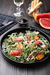 Tasty salad with arugula, cheese, grapefruit, vegetable and balsamic sauce on dark wooden table, closeup