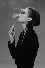 Obraz premium Black and white portrait of a stylish woman vaping with smoke in a minimalistic studio setting.