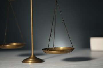 Scales of justice on light wooden table against gray background, closeup