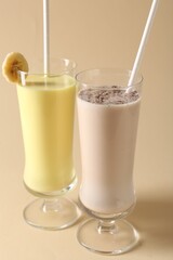 Different tasty milkshakes in glasses on beige background, closeup