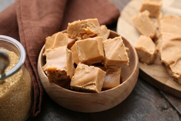 Homemade caramel candies and brown sugar on wooden table, closeup