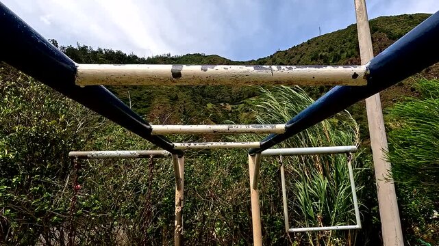 Moving along the bars of an old and worn metal play rack on a playground for children