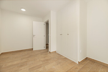 Empty hotel room with luxurious white paneled wardrobes, gold handles, and beveled mirrors integrated into the doors