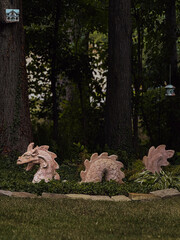 Fototapeta premium Decorative dragon sculpture appearing from the ground in a garden, surrounded by greenery and trees, creating a fantasy and magical atmosphere