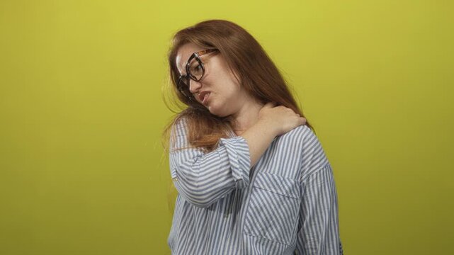 Woman wearing glasses and a striped shirt clutching her right shoulder in a bright green studio set; discomfort.