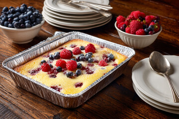 Yellow cake with red & blue berries sits on wood. Soft light shows surface details. Ideal for food product photography, recipes, or editorial.