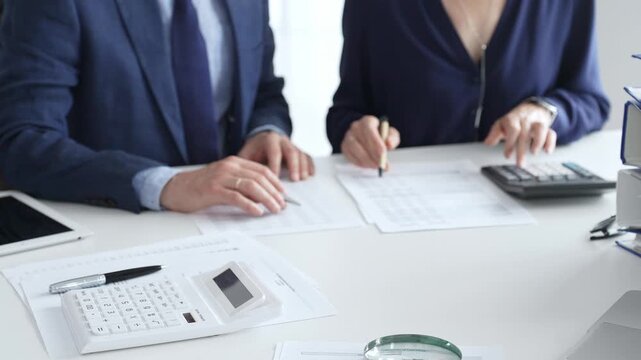 Close up of calculator and magnifying glass over financial documents opposite financial team analyzing data, reviewing reports, collaborating at modern office workspace. Audit and taxes in business - Powered by Adobe
