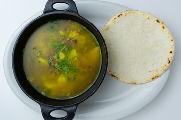 Traditional Colombian soup (Caldo), such as Caldo de Costilla or Ajiaco, a hearty homemade beef and potato broth served hot as a comforting main course in a rustic pot, isolated on a white background.
