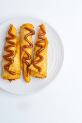 Gourmet dessert of sweet flautas or crispy pastry rolls drizzled with Arequipe (Dulce de Leche), a creative and traditional Colombian and Latin American sweet, isolated on a white background.