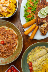 Top view of a rustic restaurant table with a variety of gourmet Colombian fusion dishes in direct sunlight, creating a warm and hearty feast.