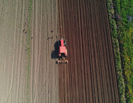 Aerial view of a red tractor plowing a field, contrasting tilled and untilled sections