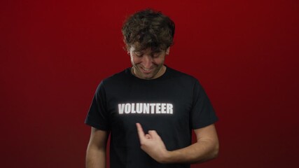 Hispanic man smiling and pointing at volunteer text on black t-shirt against a vibrant red background.