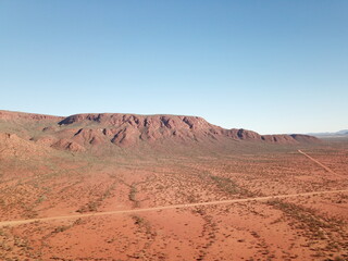 Aerial view of Mount Augustus in Western Australia, the world’s largest rock formation, rising above the red desert landscape under a clear blue sky in the remote outback.