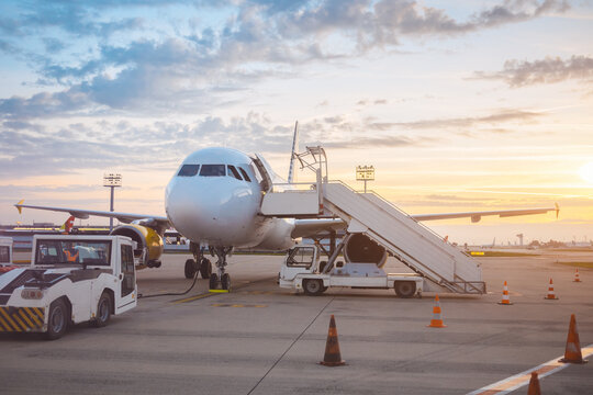 Commercial Airplane On Tarmac At Sunset With Mobile Stairs And Service Vehicles