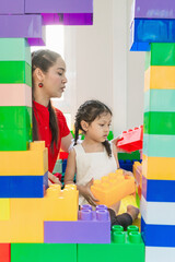 Asian mothers are teaching their daughter to learn how to play toys, creating a shape according to imagination.