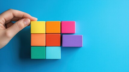 A hand holding a colorful block puzzle on a blue background.