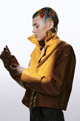 Woman with colorful artistic haircut wearing a vibrant yellow jacket, posing thoughtfully against a light background, showcasing edgy modern fashion style.