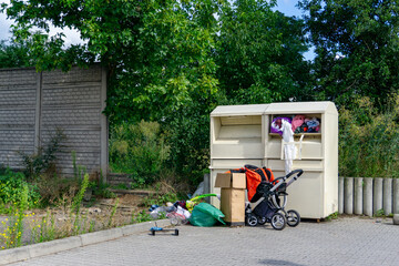 Clothing donation container by the street, with abandoned baby stroller, cardboard boxes, and...