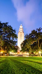Fototapeta premium Illuminated tower at dusk, framed by lush green trees and a manicured lawn