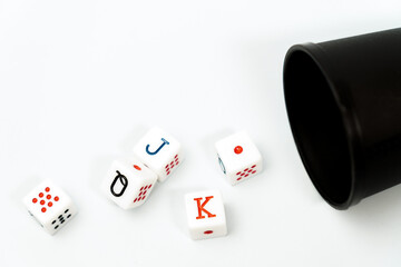 Poker dice spilling from a black dice cup onto a white background, representing gambling and games...