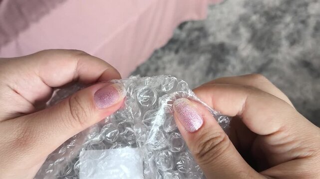 Woman bursts bubbles on a packaging bubble wrap, trying to calm down. Burst the bubbles with fingers to relieve stress