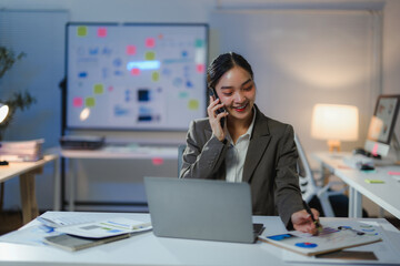 Professional manager reviewing financial data, speaking on phone, working late with laptop and charts in corporate workspace