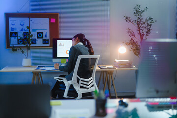 Asian businesswoman working late at night analyzing charts and graphs on computer in a modern office