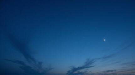Fototapeta premium Distant planet glows in deep blue twilight sky with wispy clouds stretching across horizon