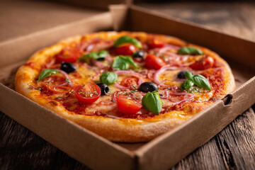 A pizza with tomatoes, olives, and onions is sitting in a cardboard box