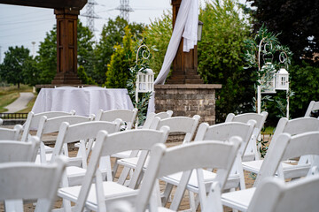Outdoor wedding ceremony setup with white chairs and lantern decorations.