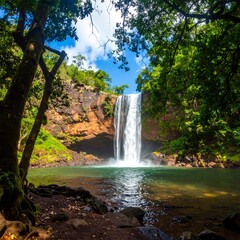 Fototapeta premium Lush green foliage frames a tall waterfall cascading into a tranquil pool
