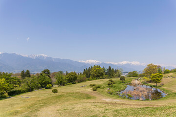 北アルプスを望むあづみ野池田クラフトパークの池と草原風景