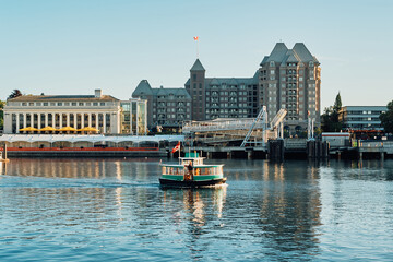 A small water taxi sailing across the harbor with the historic Fairmont Empress Hotel and nearby buildings in Victoria, Vancouver Island, Canada.