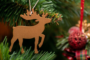 Gold deer ornament hangs on a Christmas tree. The tree is decorated with other ornaments, including a red ball. The scene conveys a festive and joyful mood