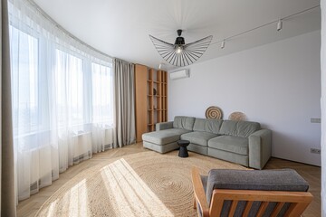 bright living room featuring a gray sofa, a round rug, a unique lamp, and large windows with sheer curtains