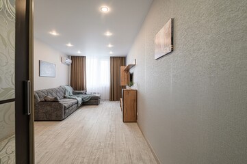 cozy living room features a grey sofa, light wood floors, a wooden media unit, and neutral-toned decor. The room is brightened by recessed lighting